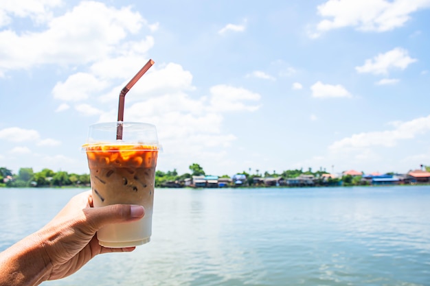 Mano che tiene un bicchiere di caffè espresso freddo con vista sul fiume e la casa. Foto Premium