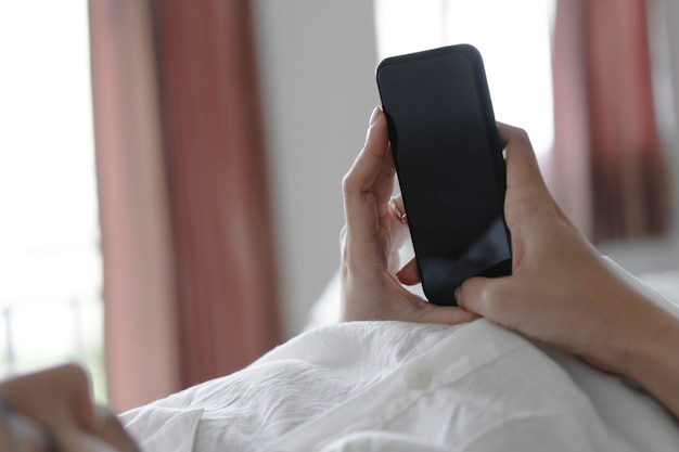 Mano della donna che utilizza smartphone con lo schermo in bianco mentre si trovava a letto al mattino. Foto Premium