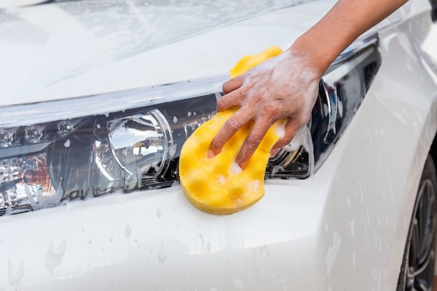 Mano della donna con l'automobile moderna del faro di lavaggio della spugna gialla o l'automobile di pulizia. Foto Premium