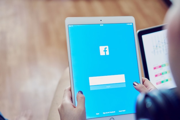 Mano sta premendo lo schermo di facebook su apple ipad pro, i social media stanno usando per informat Foto Premium