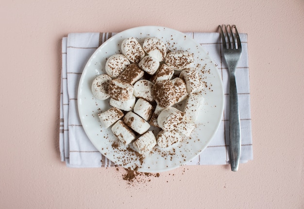 Marshmallows spolverato con cacao sul piatto bianco con forchetta sul tovagliolo. vista dall'alto di cibo dolce Foto Gratuite