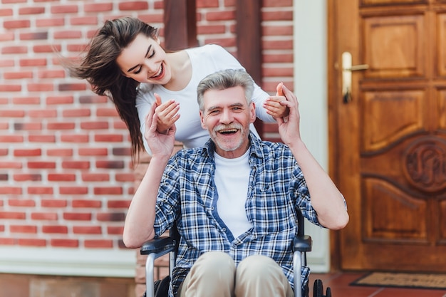 Nonno disabile allegro in sedia a rotelle che accoglie favorevolmente la sua nipote felice vicino alla casa di cura Foto Premium