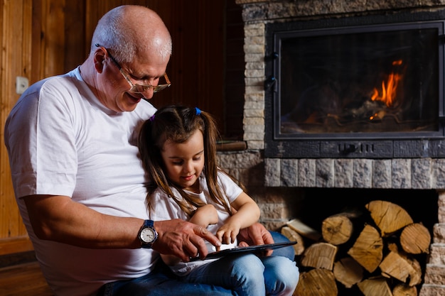 Nonno e nipote utilizzando la tavoletta di una casa vicino al camino Foto Premium