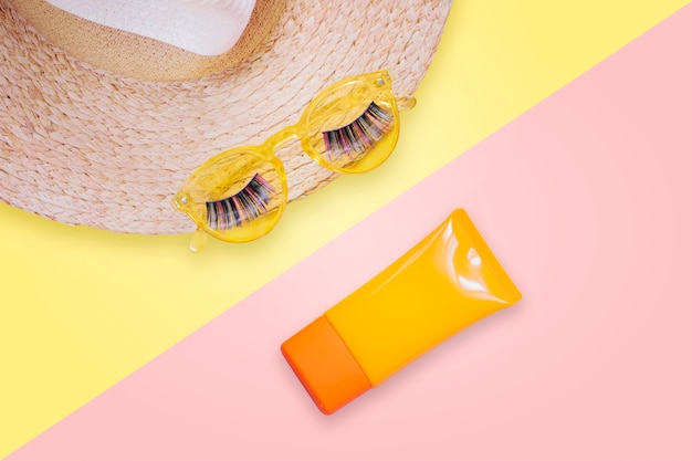 Occhiali da sole gialli con ciglia finte su cappello di paglia e crema solare spf crema su sfondo rosa. Foto Premium