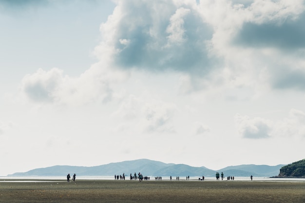 Paesaggio di bassa marea con montagna verde, cielo nuvola con sagome di persone Foto Premium