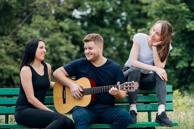 Persone contente seduto sulla panchina e suonare la chitarra Foto Gratuite
