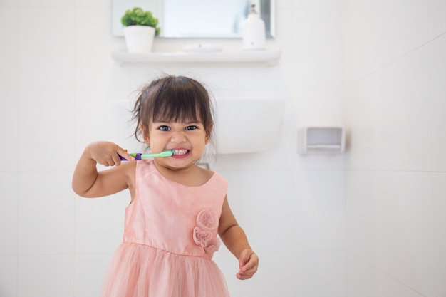 Piccola neonata sveglia che pulisce i suoi denti con lo spazzolino da denti nel bagno Foto Premium