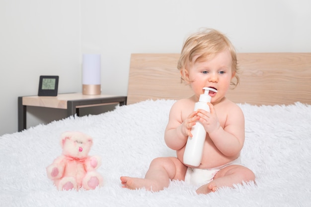 Piccola neonata sveglia con la bottiglia di olio per bambini nella camera da letto del genitore. Foto Premium