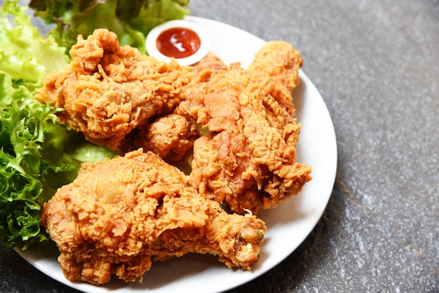 Pollo fritto croccante sul piatto bianco con la verdura della lattuga dell'insalata e del ketchup sul piatto scuro Foto Premium