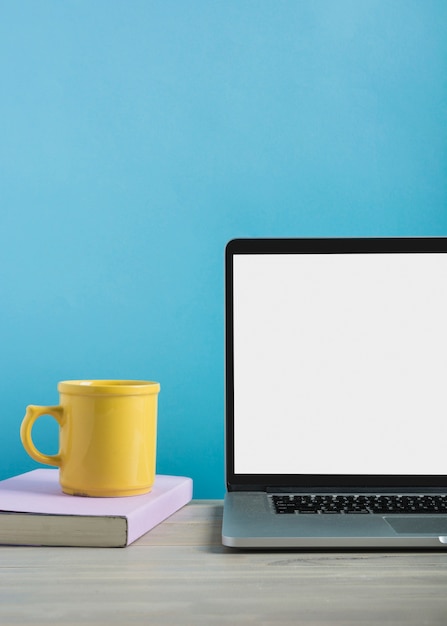 Primo piano del computer portatile con la tazza di caffè e libro sullo scrittorio di legno Foto Gratuite