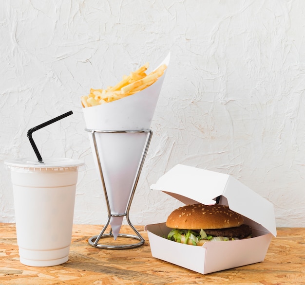 Primo piano di hamburger; patatine fritte e tazza di smaltimento sulla scrivania in legno Foto Gratuite