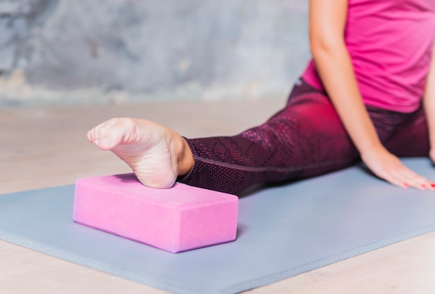 Primo piano di una donna di forma fisica che allunga la gamba utilizzando il blocco di yoga rosa Foto Gratuite