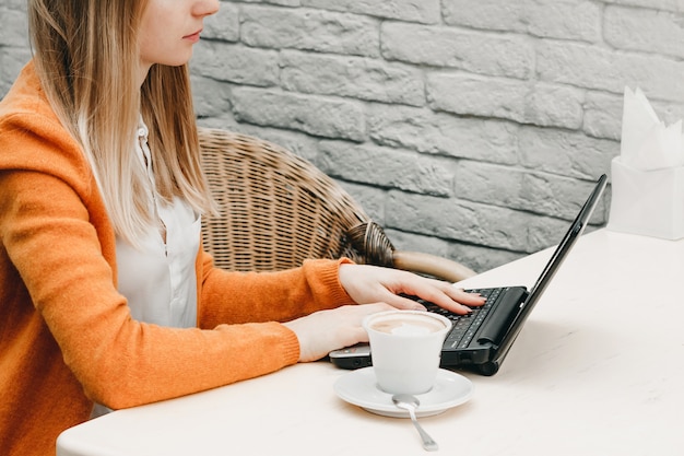 Ragazza bionda in un caffè con un computer portatile e caffè. free lance della ragazza che lavorano ad un computer portatile Foto Premium
