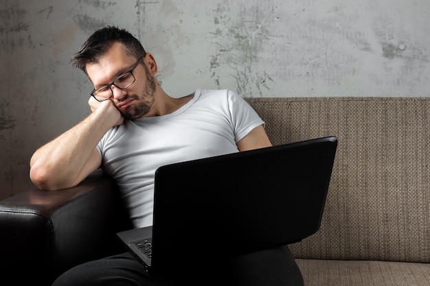 Ragazzo che indossa una camicia bianca seduto sul divano, si addormentò al lavoro su un computer portatile. Foto Premium