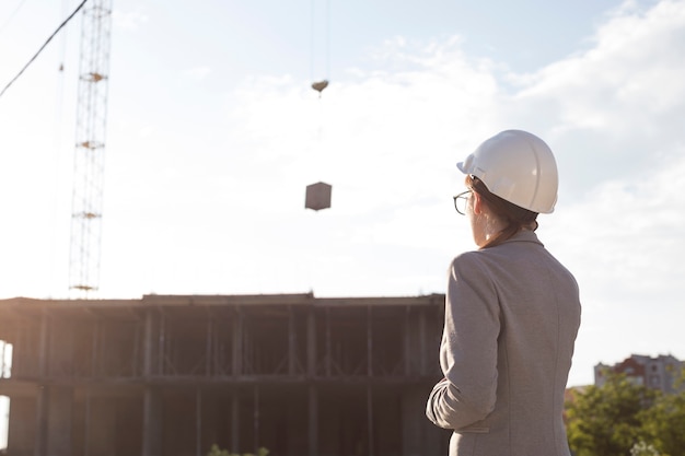 Retrovisione dell'architetto femminile che porta il cappello del cervo maschio che esamina cantiere Foto Gratuite