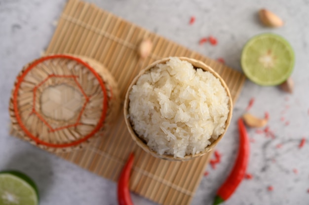 Riso appiccicoso tailandese in un canestro di bambù tessuto su un pannello di legno con i peperoncini rossi, la calce e l'aglio Foto Gratuite
