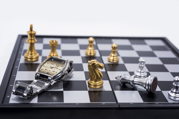 Scacchiera su figure bianche, dorate e argentate con orologio a mano Foto Premium