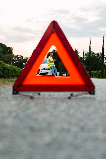 Segno rosso di arresto di emergenza e giovane che aspettano l'assistenza dell'automobile con l'automobile rotta sulla strada Foto Premium