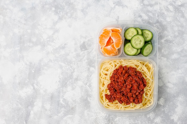 Spaghetti alla bolognese da asporto in una scatola di pranzo in plastica e fetta di frutta sulla luce Foto Gratuite