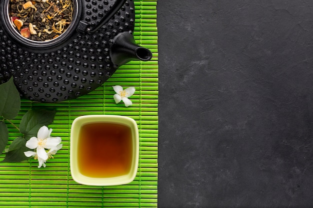 Tè sano con erbe secche e fiori di gelsomino bianchi su tovaglietta verde su sfondo nero Foto Gratuite