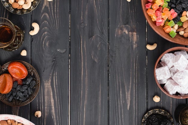 Tè turco; frutta secca; uva passa; noci e lukum sulla scrivania in legno con texture nera Foto Gratuite