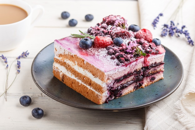 Torta di bacche con crema di latte e marmellata di mirtilli sul piatto in ceramica blu con tazza di caffè e mirtilli freschi. vista laterale Foto Premium