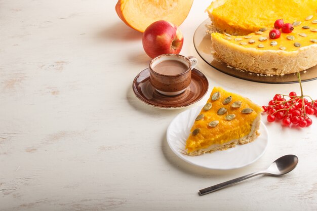 Torta di zucca dolce americana tradizionale decorata con le bacche e i semi di zucca rossi del biancospino con la tazza di caffè su un bianco di legno. vista laterale. Foto Premium