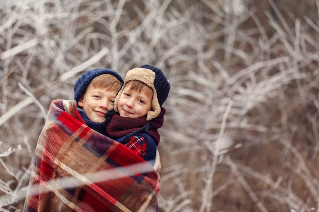 Un abbraccio di due amici dei ragazzini sotto la coperta calda nella foresta di inverno. . fratello amore. amicizia di concetto Foto Premium
