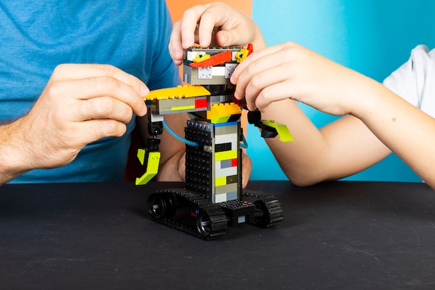 Un uomo e un ragazzo si riuniscono da un costruttore di un robot. le mani maschili e dei bambini raccolgono lego Foto Premium