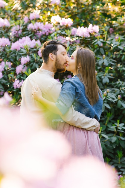 Una giovane coppia in amore ragazzo e ragazza bacio sullo sfondo di un rododendro in fiore. primo appuntamento. san valentino Foto Premium