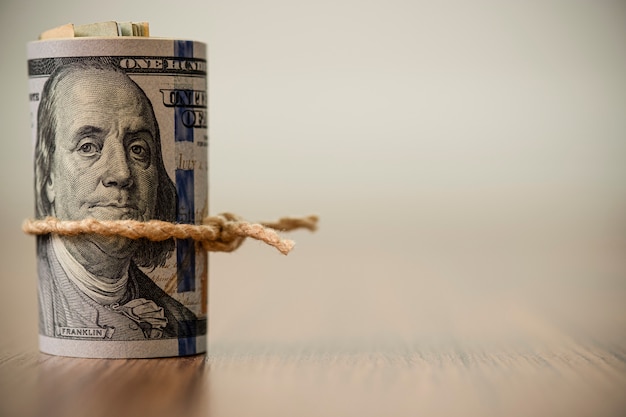 Una macro di un rotolo di 100 banconote del dollaro americano sullo spazio di legno della copia e del fondo Foto Premium
