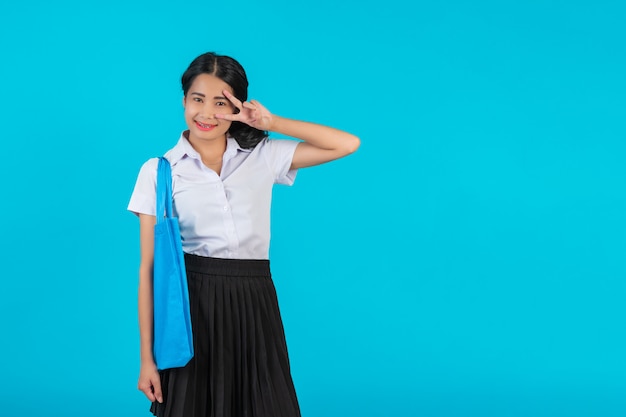 Una studentessa asiatica che gira una borsa di stoffa e mostra vari gesti su un blu. Foto Gratuite