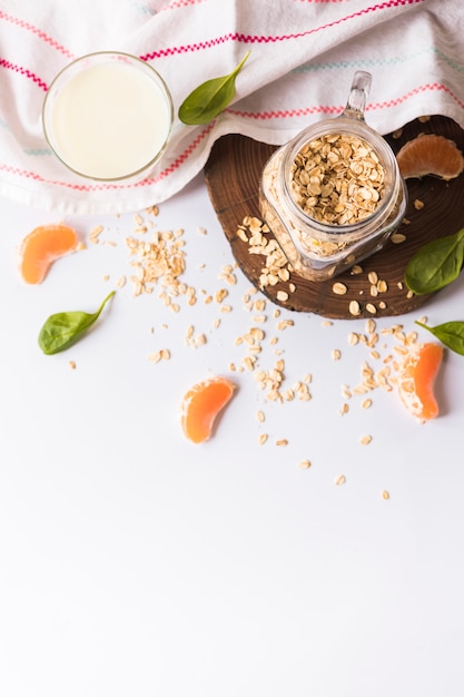 Una visione elevata del latte; foglie di basilico; avena; fette d'arancia e tovagliolo su sfondo bianco Foto Gratuite