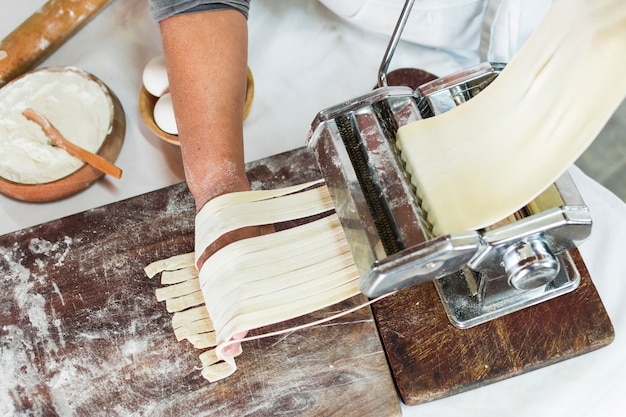 Una vista dall'alto del fornaio taglio di pasta cruda in tagliatelle su macchina per la pasta Foto Gratuite
