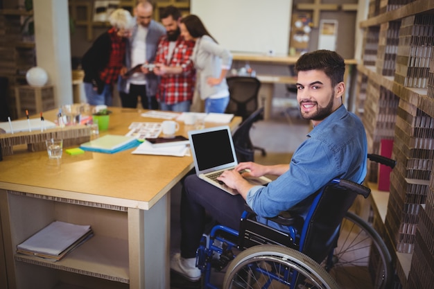 Uomo d'affari disabile sicuro che per mezzo del computer portatile allo scrittorio Foto Premium