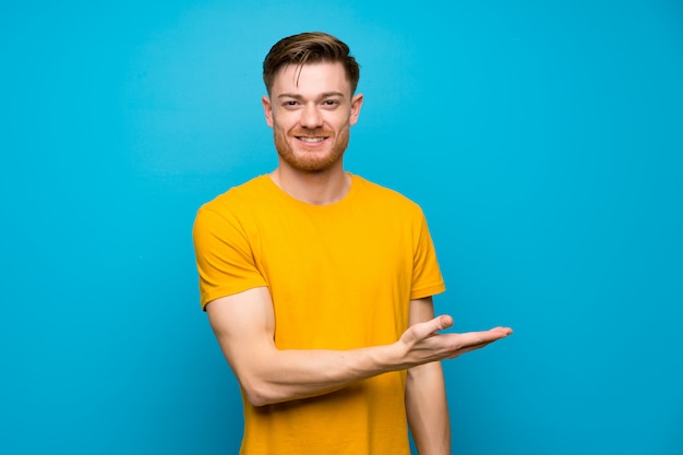 Uomo della testarossa sopra la parete blu che presenta un'idea mentre guardando sorridendo verso Foto Premium