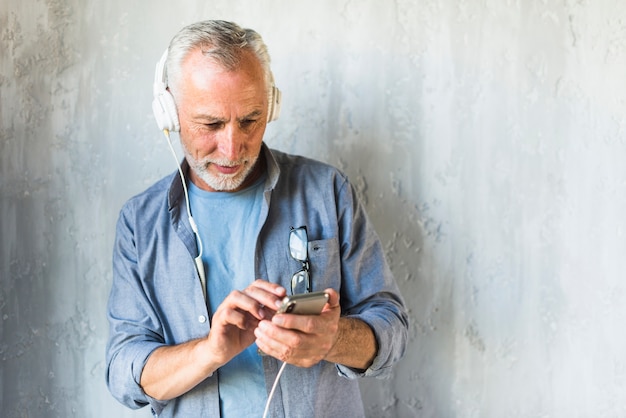 Uomo senior che sta davanti alla musica d'ascolto del muro di cemento sulla cuffia Foto Gratuite