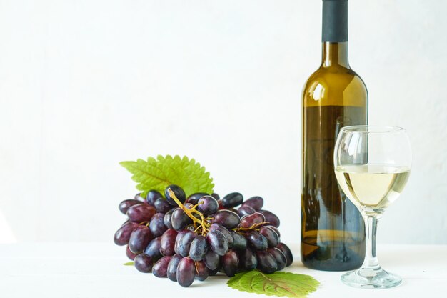 Uva nera con un bicchiere di vino bianco e una bottiglia di vino su un tavolo luminoso Foto Premium