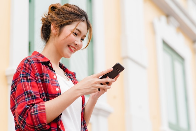 Viaggiatore con zaino e sacco a pelo turistico della donna asiatica che sorride e che usando smartphone che viaggia da solo Foto Gratuite