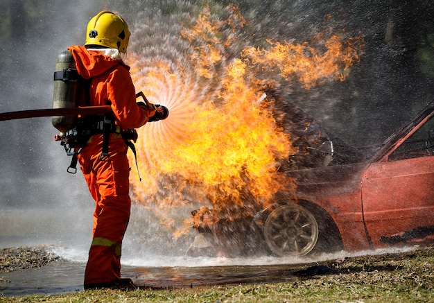 Vigile del fuoco che hosing l'acqua per estinguere un fuoco sopra l'automobile nell'incidente Foto Premium