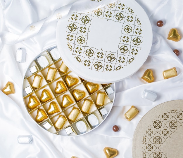 Vista dall'alto della scatola rotonda di cioccolato con cioccolatini avvolti d'oro e d'argento Foto Gratuite