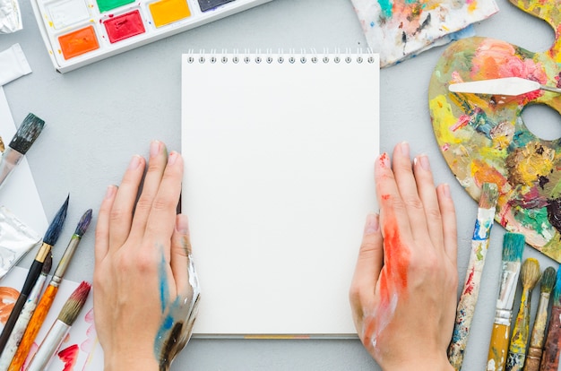 Vista dall'alto mani con notebook circondato da elementi di pittura Foto Gratuite