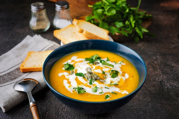 Zuppa di zucca con panna e prezzemolo sul tavolo rustico scuro Foto Premium