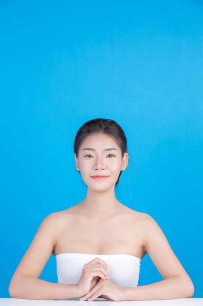 A beleza das mulheres com imagens perfeitas de saúde da pele tocando em seu rosto e sorrindo como um spa para cuidar de sua pele azul Foto gratuita