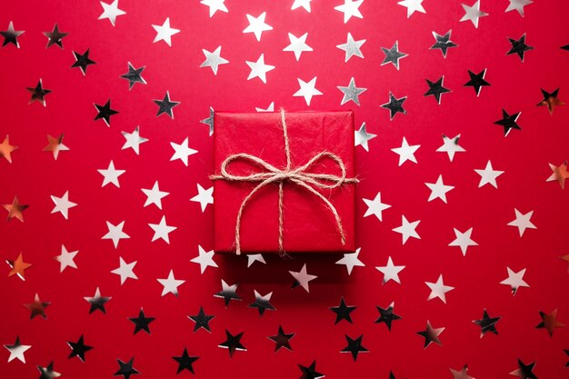 A caixa de presente vermelha do natal com estrela de prata polvilha no backgound vermelho. lay plana. Foto Premium