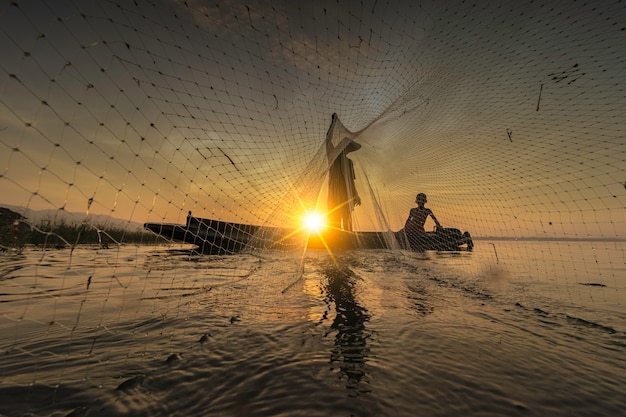 A imagem é silhueta. os pescadores estão saindo para pescar no início da manhã com barcos de madeira, lanternas antigas e redes. estilo de vida do pescador de conceito. Foto Premium