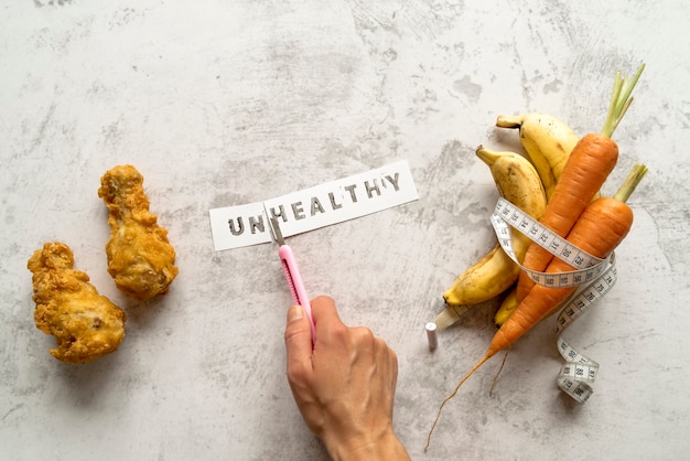 A mão da pessoa que corta a palavra insalubre perto do frango frito com banana e cenouras rolou na fita de medição Foto gratuita