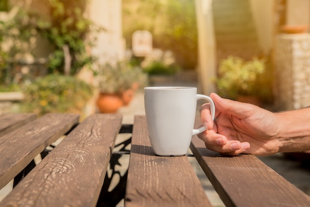 A mão está segurando uma xícara de café.men estão bebendo café da manhã com um fundo verde lá fora. man mãos segurando xícara de café no café ao ar livre verão Foto gratuita