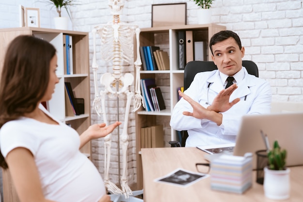 A menina grávida e o doutor falam seriamente no escritório do doutor Foto Premium