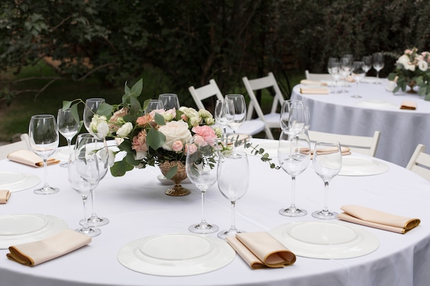 Ajuste da tabela do casamento decorado com flores frescas em um vaso de bronze. mesa de banquete para os hóspedes ao ar livre com vista para a natureza verde Foto Premium